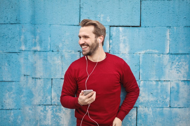 Usmívající se muž držící mobil se sluchátky na uších